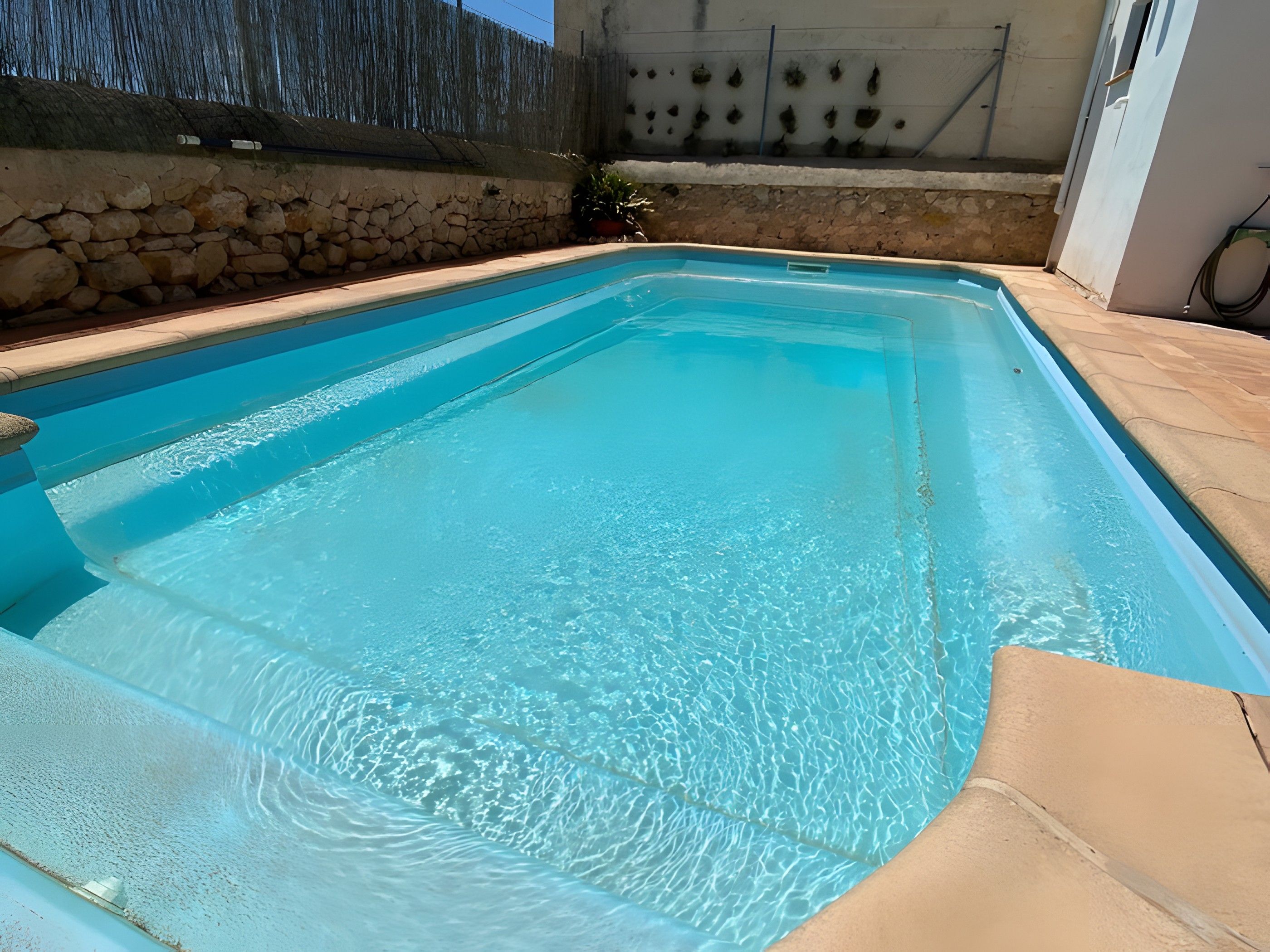 Une piscine rectangulaire à l’eau d’un bleu cristallin, entourée de murs en pierre et bordée d’une terrasse carrelée.