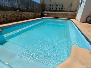 Ein rechteckiger Pool mit klarem, blauem Wasser, umgeben von Steinmauern und einer gefliesten Liegefläche.
