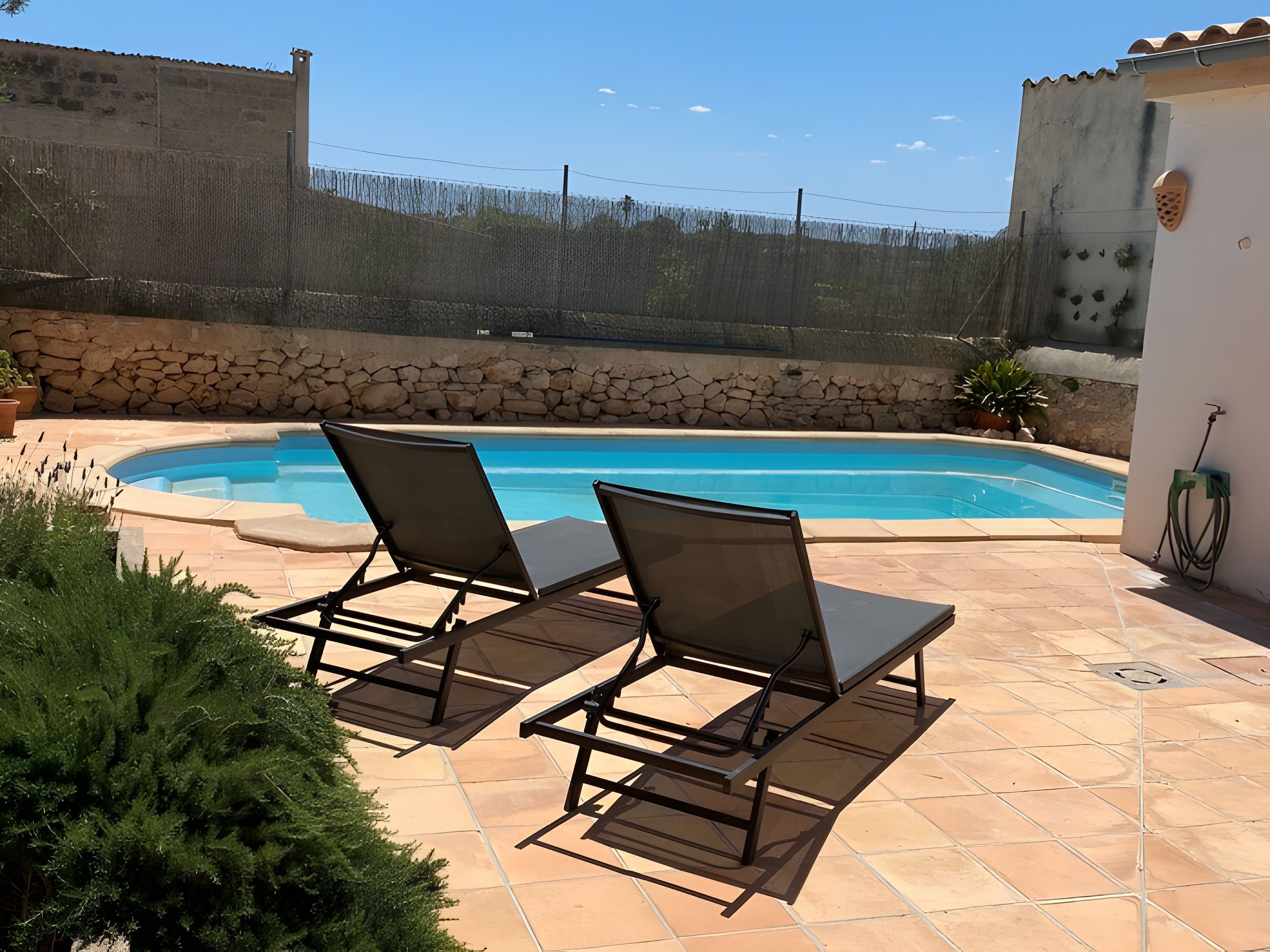 A swimming pool with two lounge chairs and a stone wall in the background.