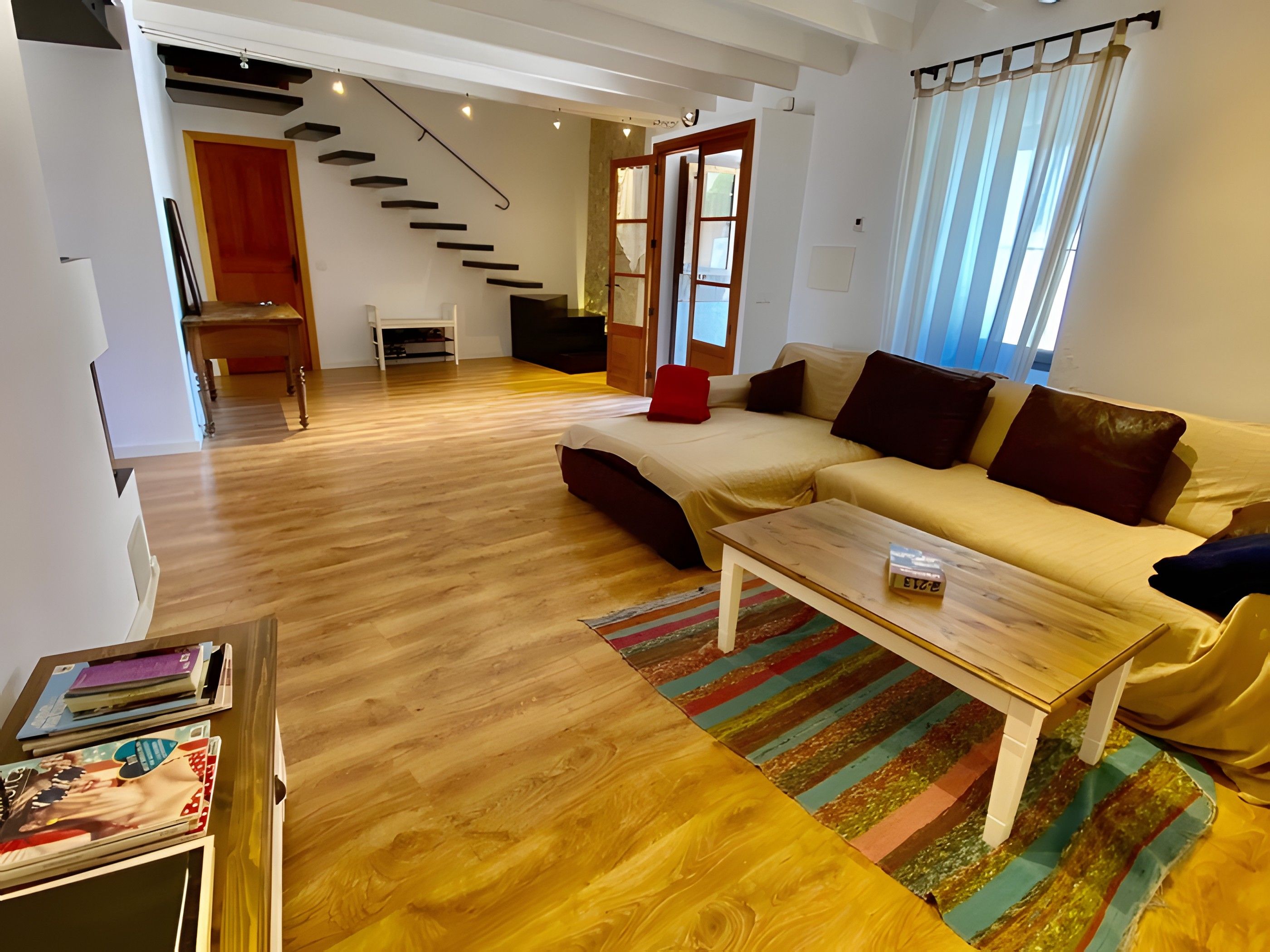 A modern living room with a sofa, a coffee table, and a staircase leading to another room.