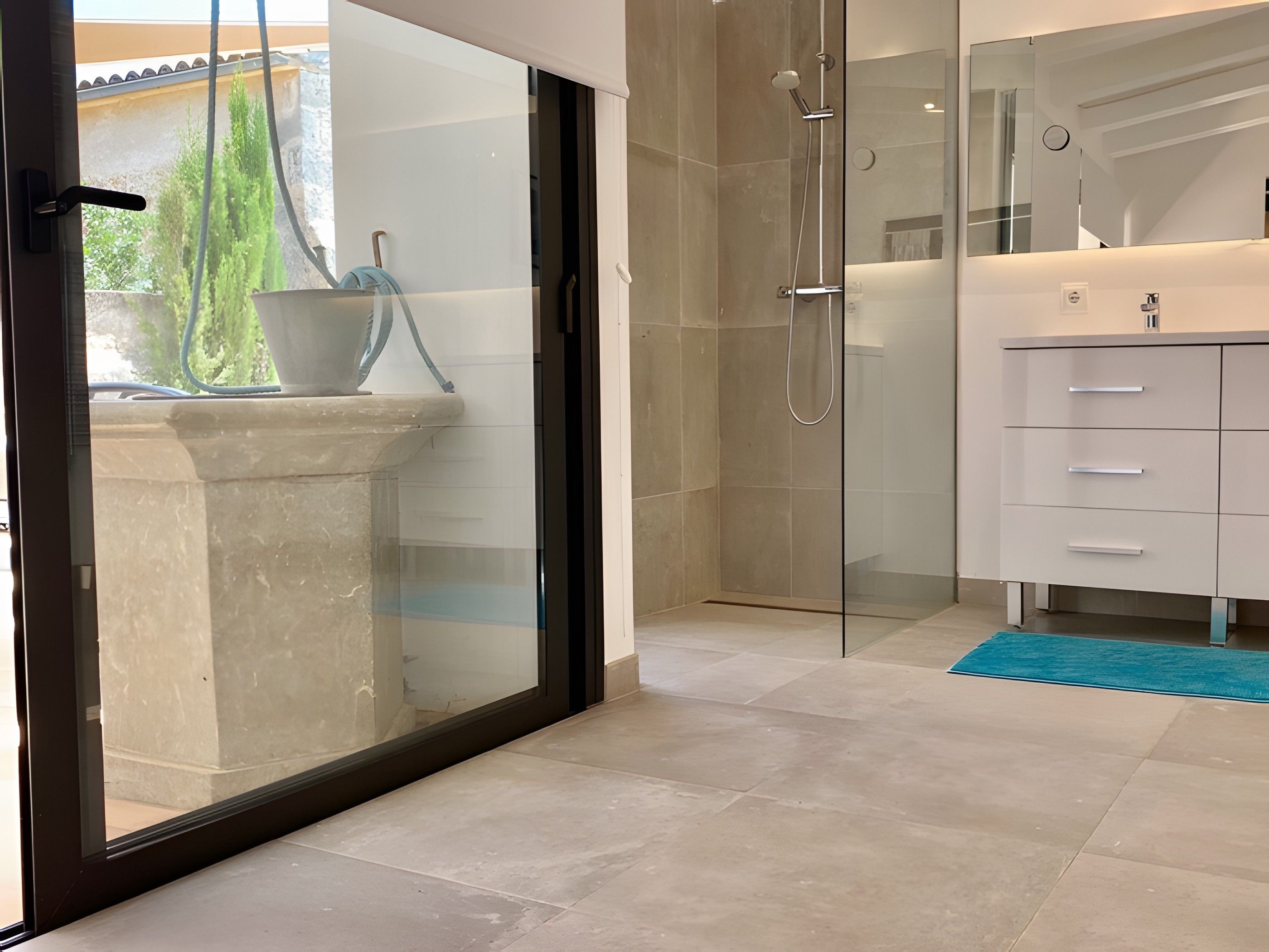 Une salle de bain moderne avec une douche à parois de verre, un lavabo blanc et un tapis bleu.