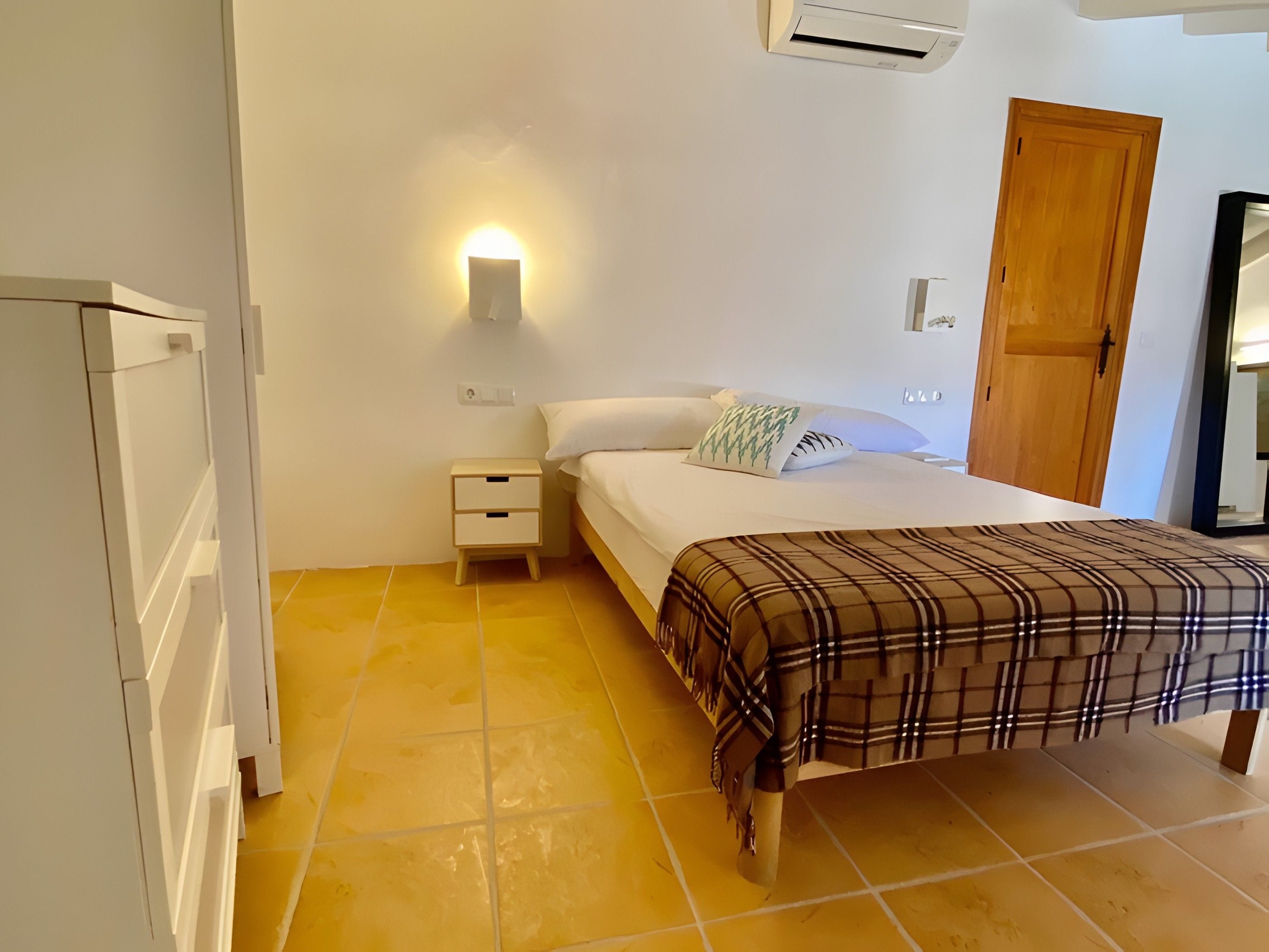 Une chambre à coucher comprenant un lit, une table de chevet, une commode et une lampe fixée au mur.