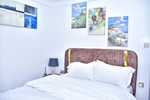 Une chambre d’hôtel comprenant un lit, une table de chevet et des œuvres d’art murales, notamment un tableau représentant un phare.