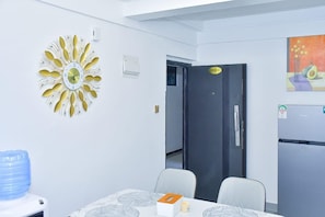 Een kamer met een unieke zonvormige klok, een deur met een bordje, een koelkast en een waterdispenser.
