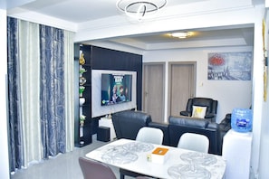 Een moderne woonkamer met een flatscreen televisie, een eethoek met tafel en stoelen, en een waterdispenser.