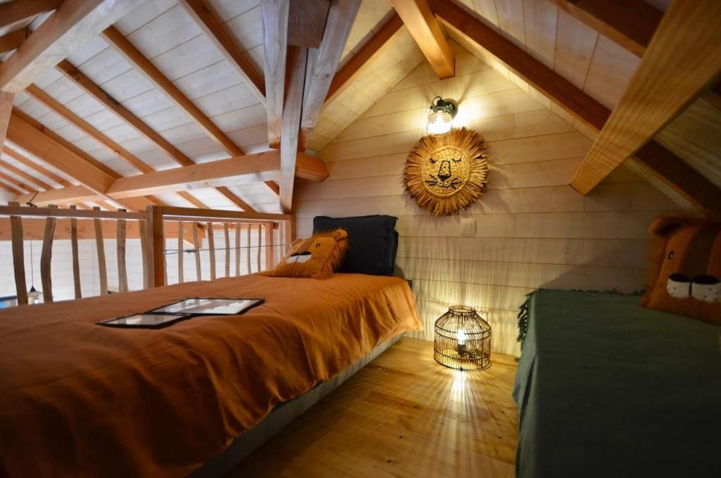 Un dormitorio con techo inclinado, una cama con colcha naranja, una mesita de noche con lámpara y un aplique de pared.