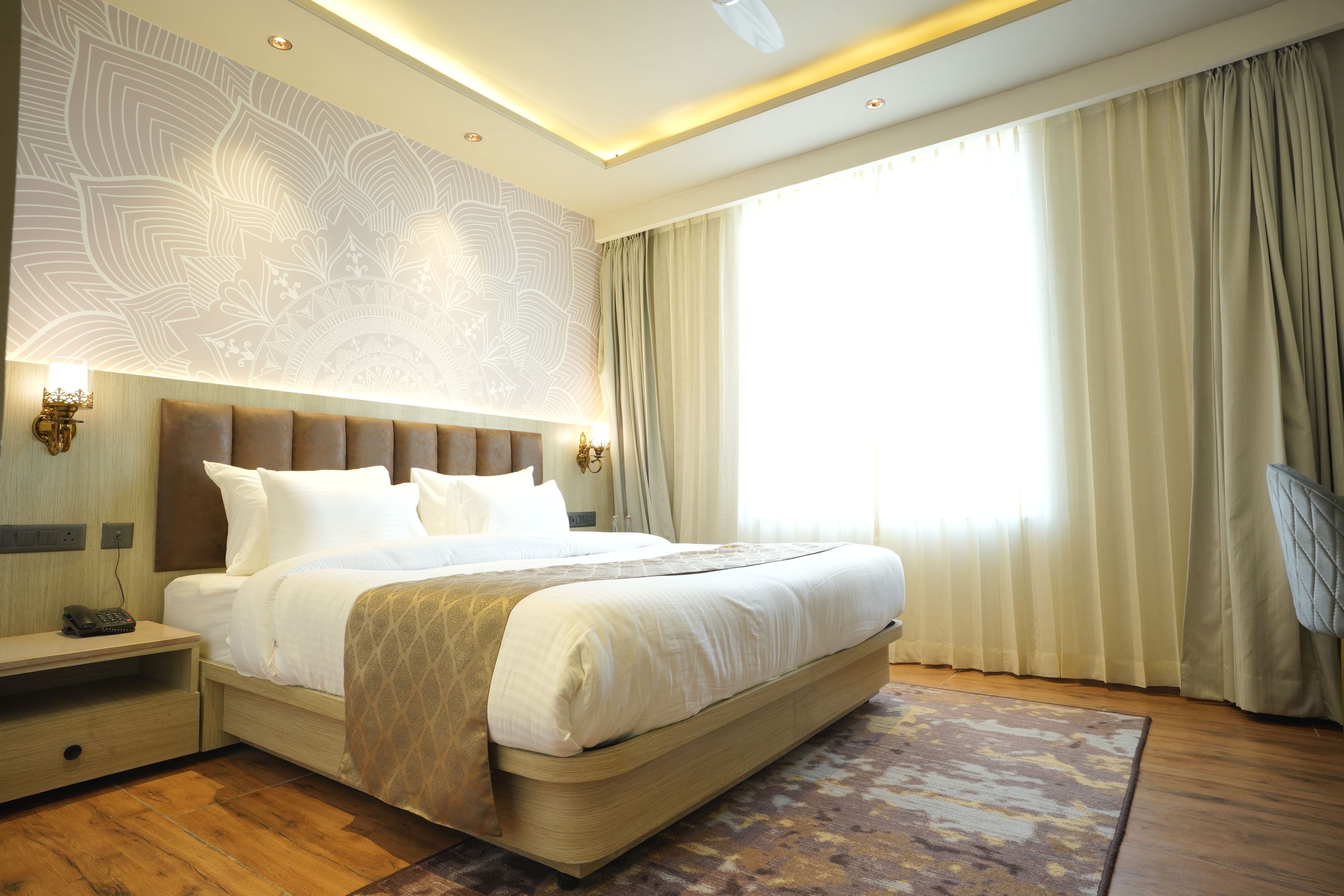 Quarto de hotel moderno com uma cama grande, mesa de cabeceira, escrivaninha e uma janela ampla com cortinas.