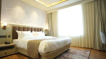 Quarto de hotel com cama grande, mesa de cabeceira, luminária na parede e janela com cortinas.