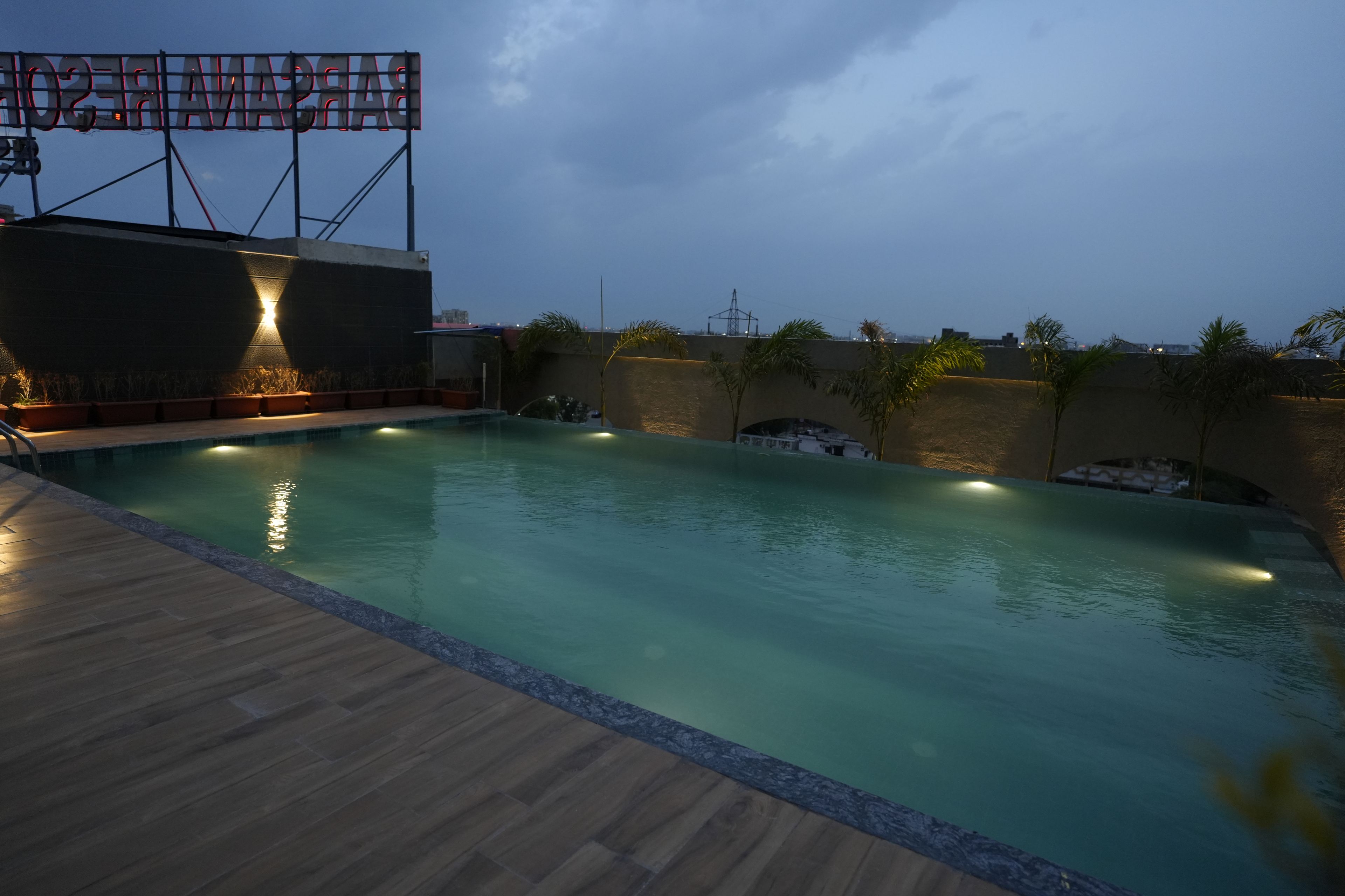 A swimming pool with a wooden deck, surrounded by walls with plants and a large illuminated sign.