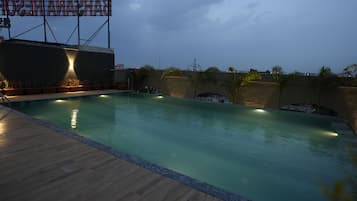 Piscina com deck de madeira, cercada por paredes com plantas e um grande letreiro iluminado.