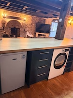 Una cocina funcional con lavadora integrada, una pared de piedra y un televisor.
