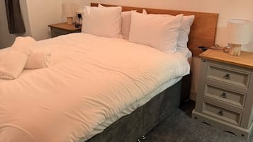 Una cama bien hecha con sábanas blancas, un cabecero de madera y dos mesitas de noche con lámparas.