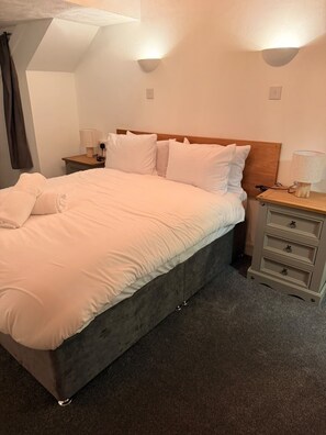 A neatly made bed with white linens, a wooden headboard, and two bedside tables with lamps. - Crumplehorn Inn & Mill (Looe)