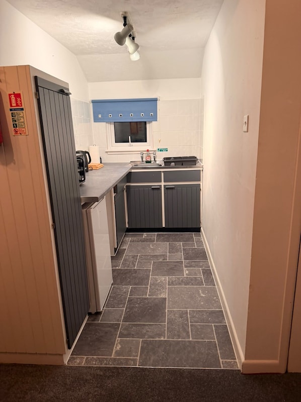 A narrow hallway leading to a kitchen with a blue window, a sink, and a kettle. - Crumplehorn Inn & Mill (Looe)