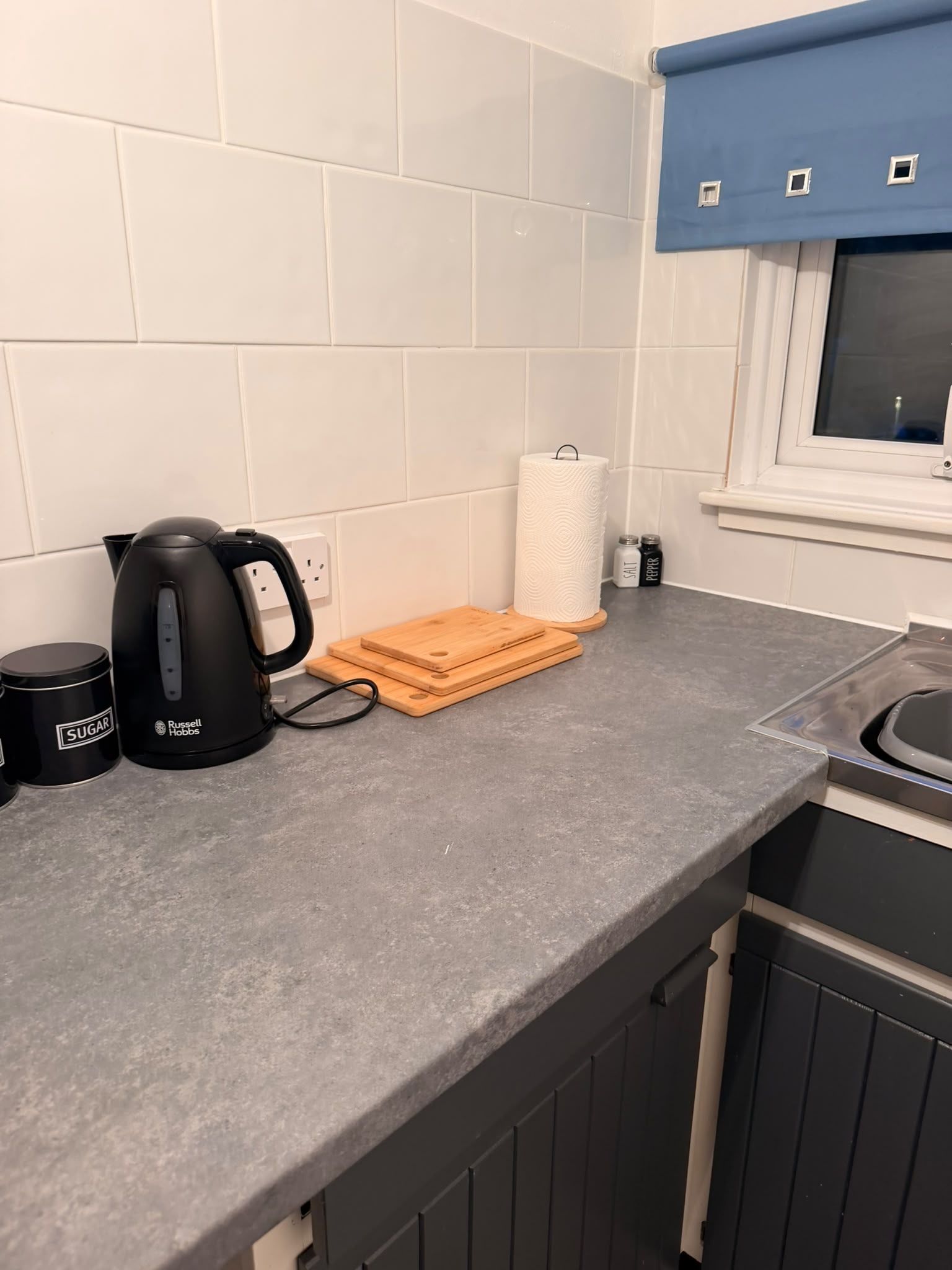 Una cocina con hervidor, tabla de cortar, saleros y pimenteros, y una taza de café.