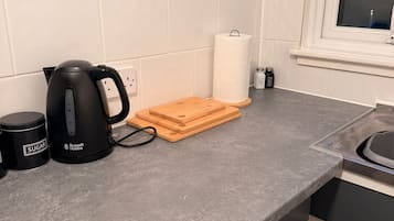 Una cocina con hervidor, tabla de cortar, saleros y pimenteros, y una taza de café.