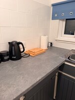 Una cocina con hervidor, tabla de cortar, saleros y pimenteros, y una taza de café.