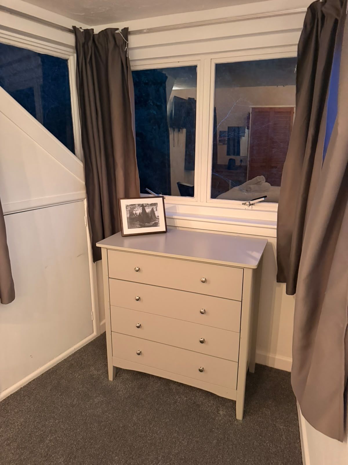 Una habitación con ventana, un escritorio con cajones y cortinas.