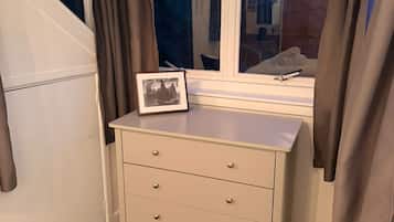 Una habitación con ventana, un escritorio con cajones y cortinas.