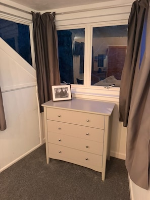 A room with a window, a desk with drawers, and curtains.