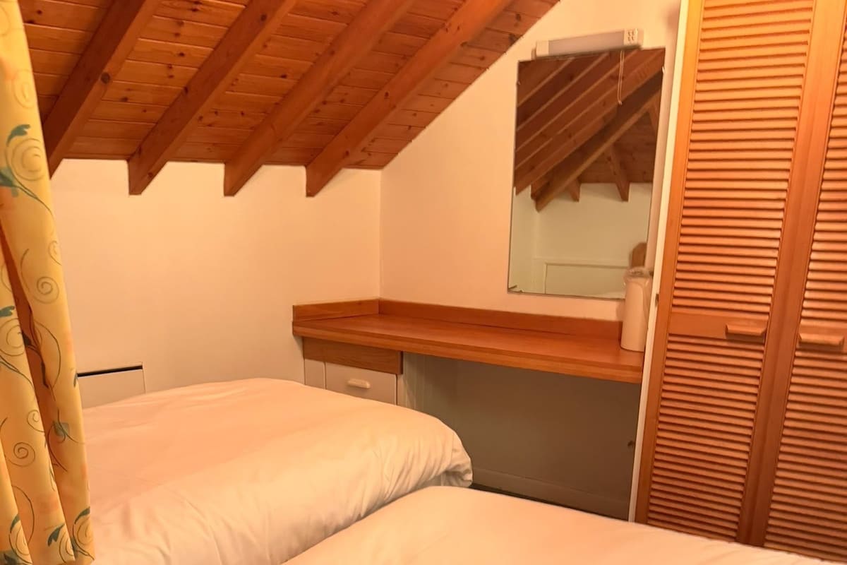 Un dormitorio con dos camas individuales, vigas de madera en el techo, una mesita de noche de madera, un espejo y un armario.
