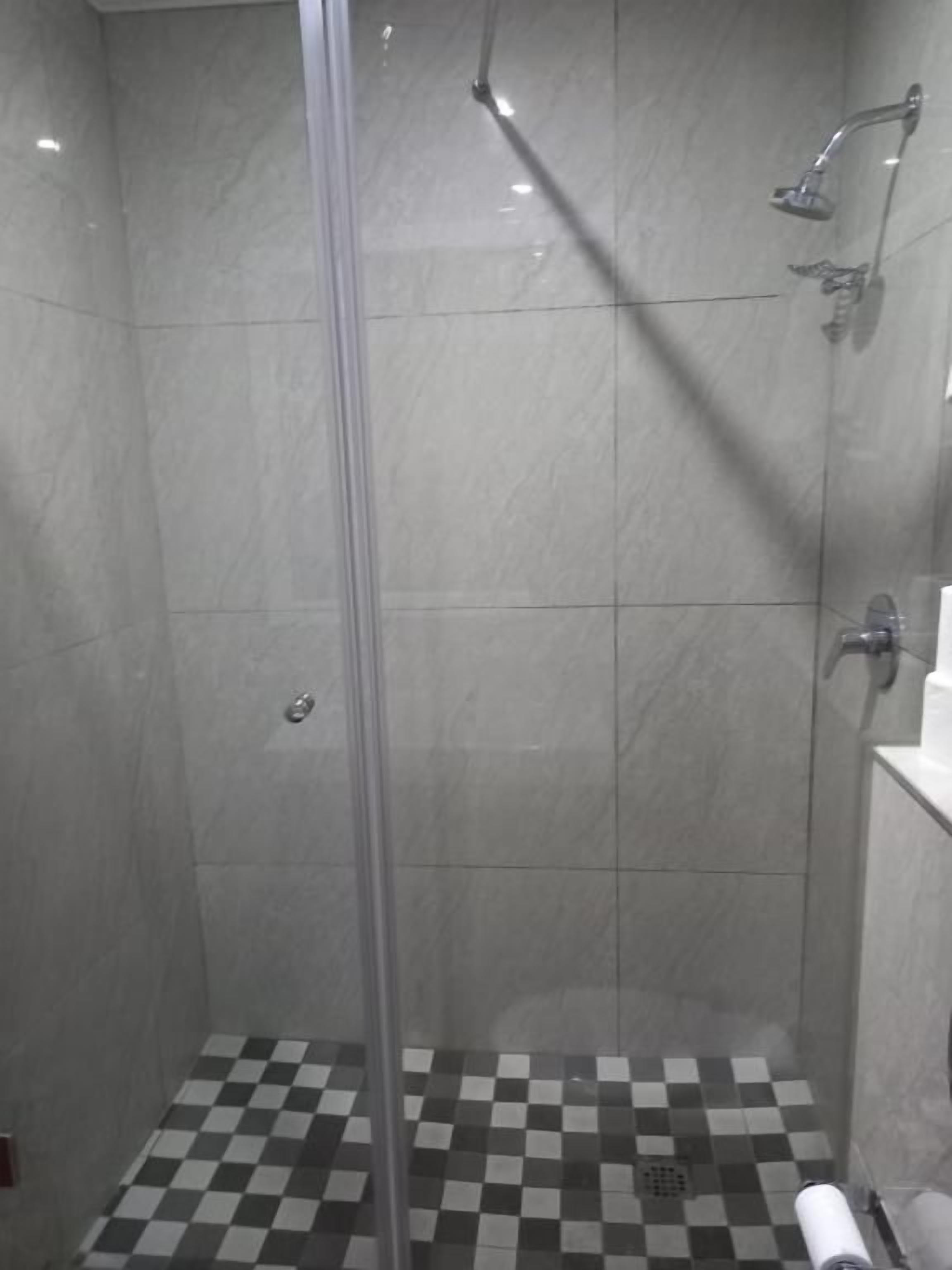 A shower with a glass door, a checkered floor, and a wall-mounted faucet.