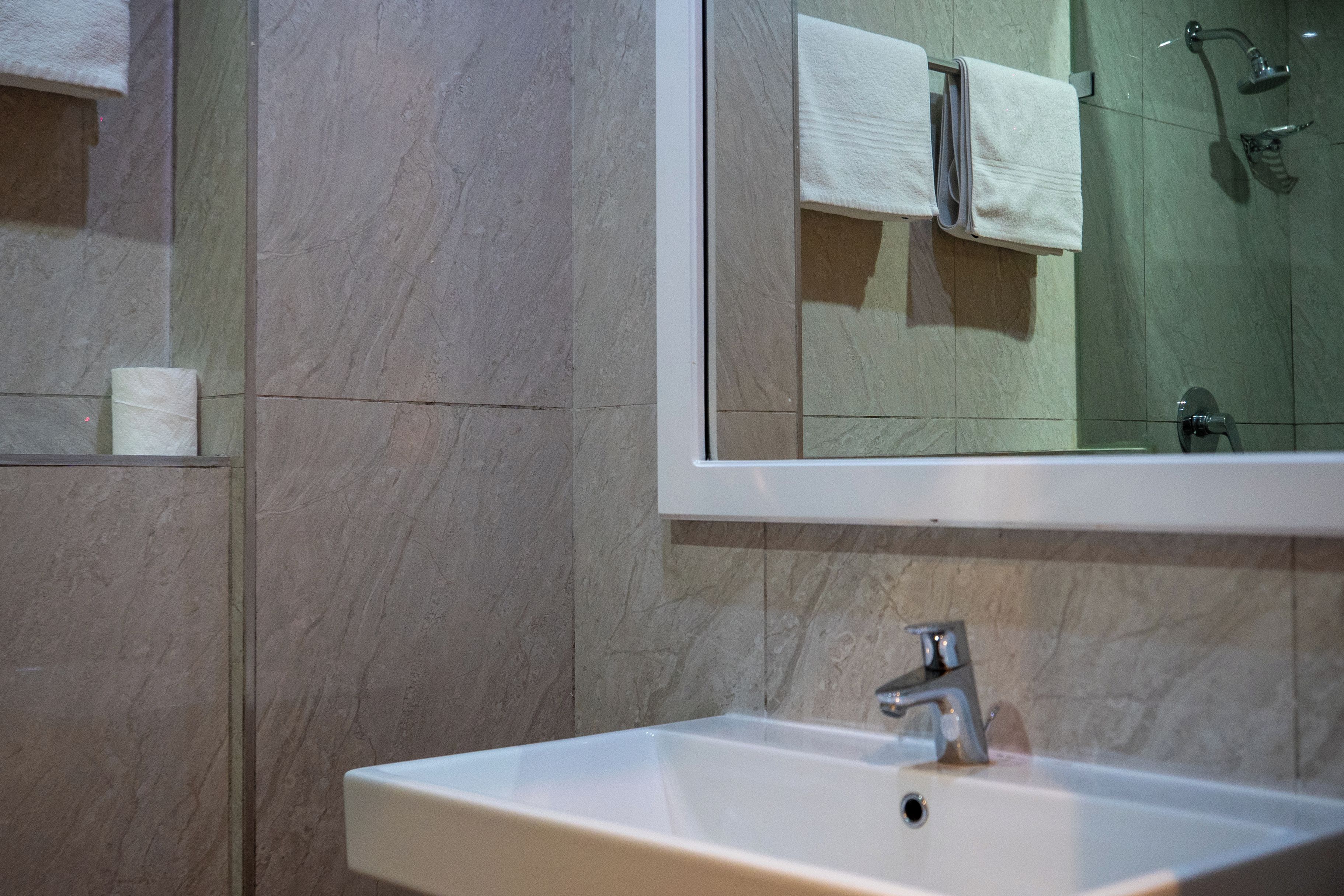 A bathroom with a white sink, a mirror above it, and a shower area in the reflection.
