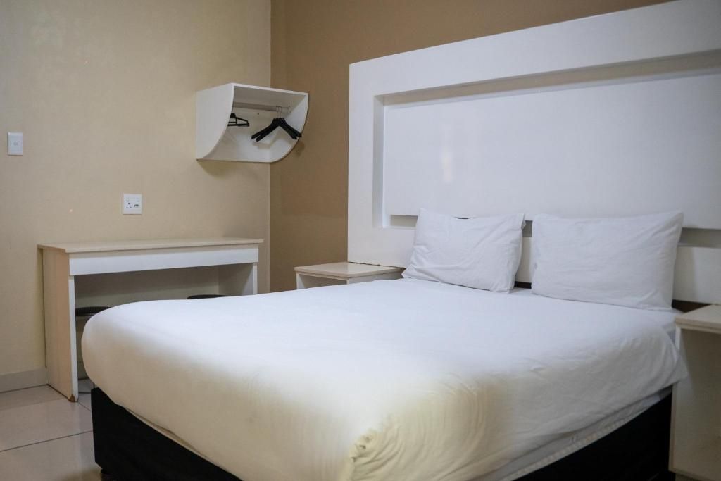 Habitación de hotel con cama, mesita de noche y un armario empotrado con ropa colgada.