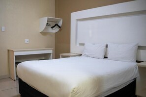 Habitación de hotel con cama, mesita de noche y un armario empotrado con ropa colgada.