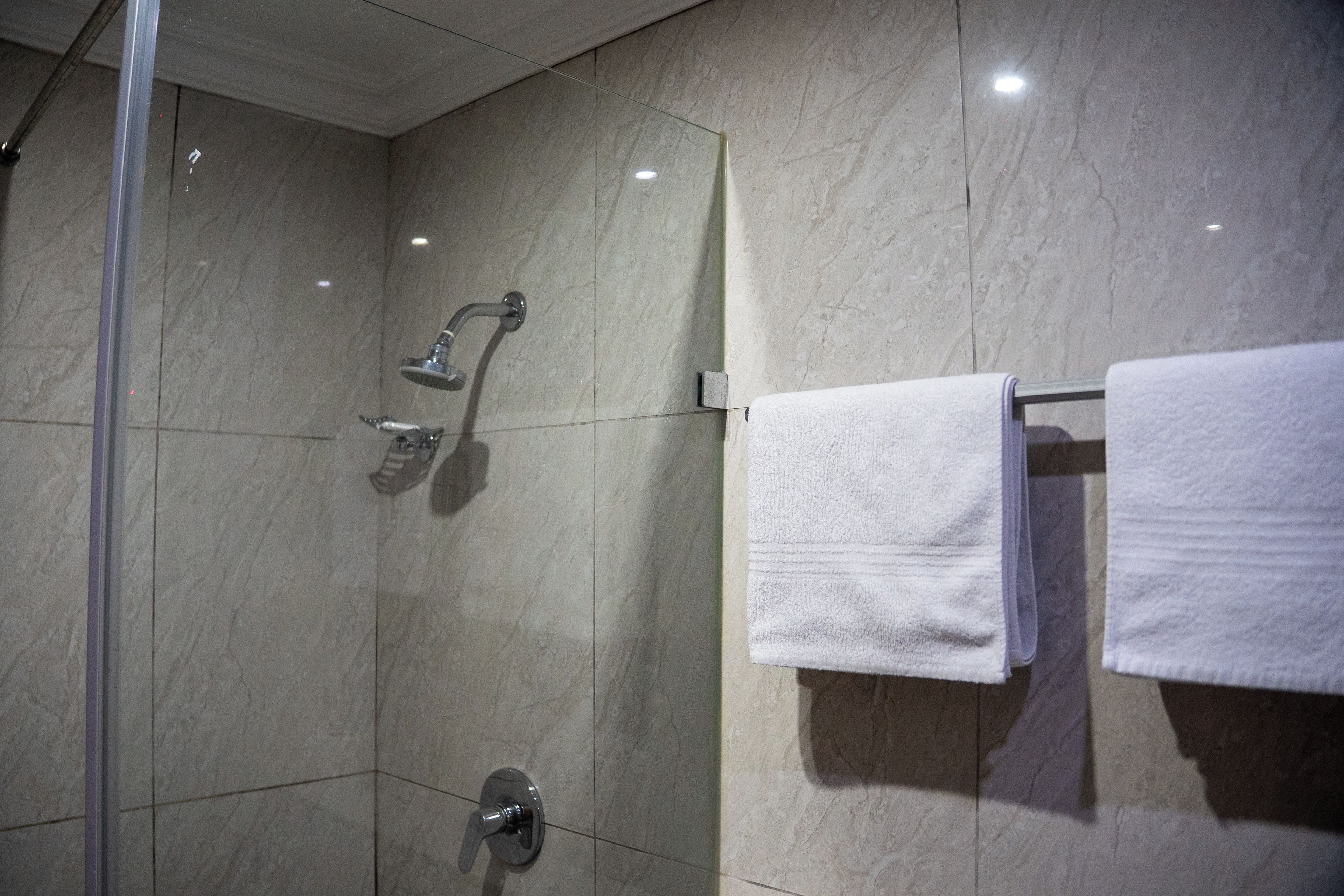 Un baño moderno con cabina de ducha de vidrio, cabezal de ducha manual y un perchero con dos toallas.