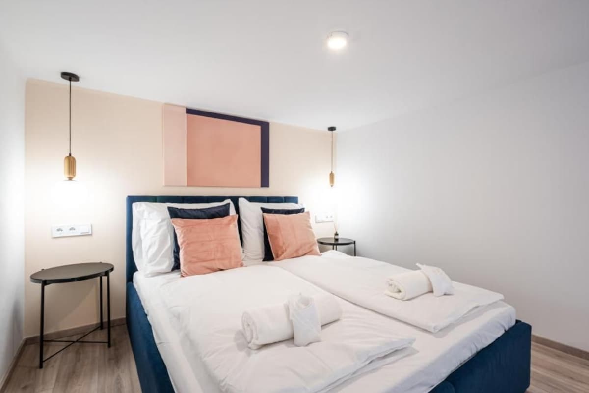 Habitación de hotel con cama, dos mesitas de noche, luz de pared y luz de techo.