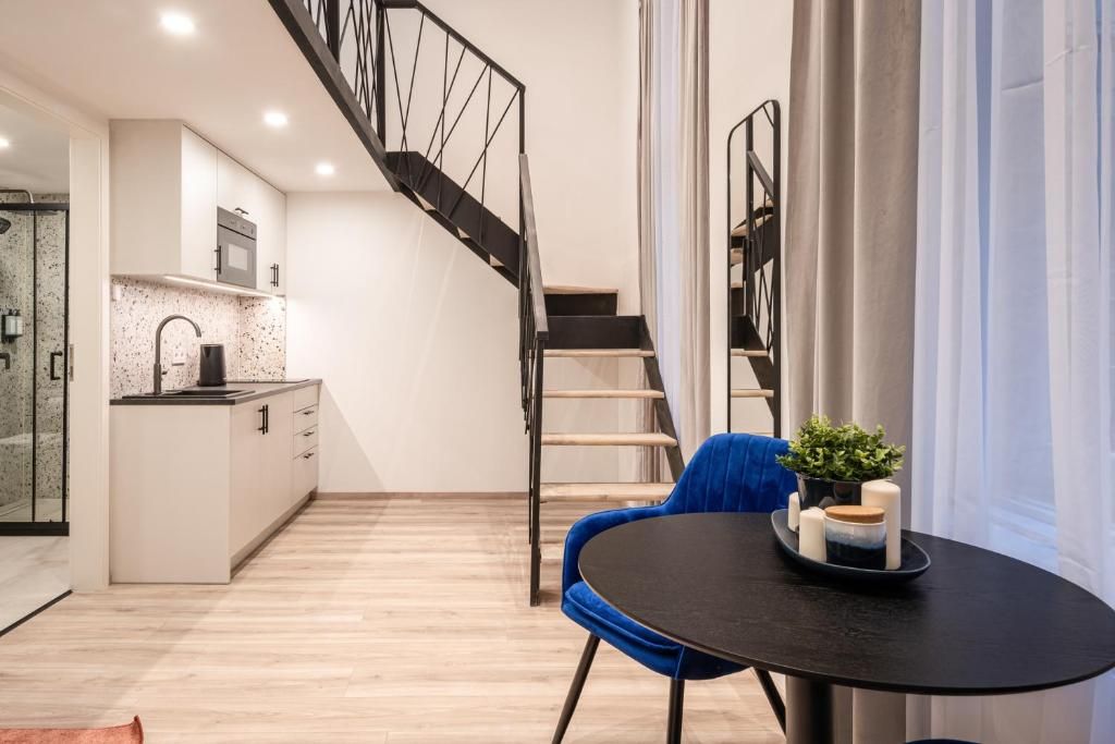 Eine moderne Küche mit eingebautem Backofen und Mikrowelle, eine Essecke mit einem schwarzen Tisch und einem blauen Stuhl sowie eine Treppe mit Metallgeländer.
