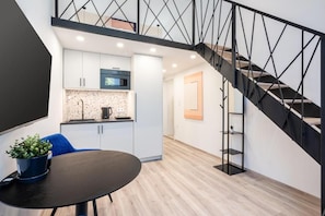 Eine moderne Küche mit weißen Schränken, einer Mikrowelle und einem Spülbecken. Eine Treppe mit schwarzer Metallreling führt auf eine obere Ebene.