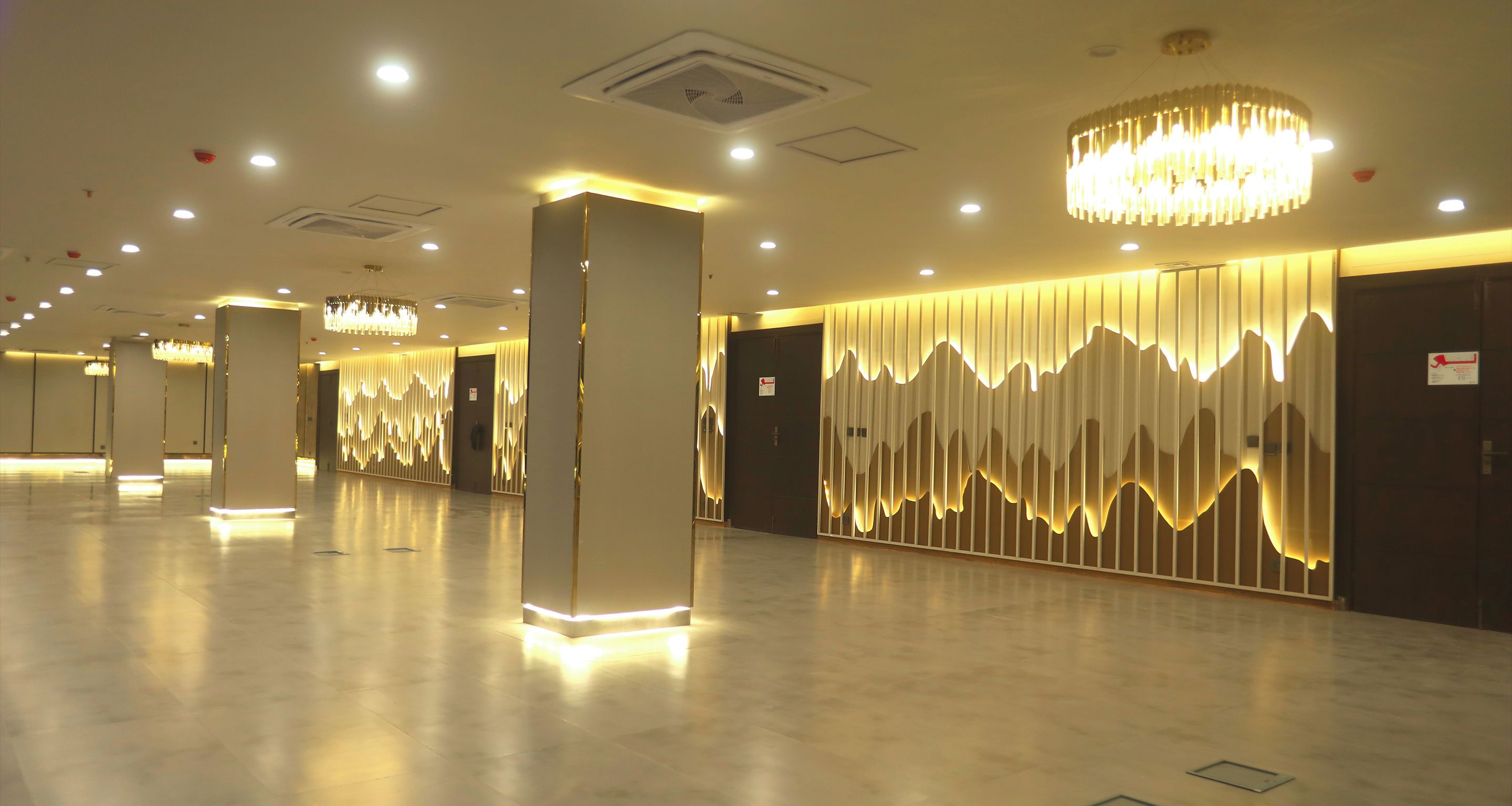Un amplio vestíbulo de hotel con diseño moderno, que presenta una larga recepción, una pared decorativa con iluminación vertical y una araña.