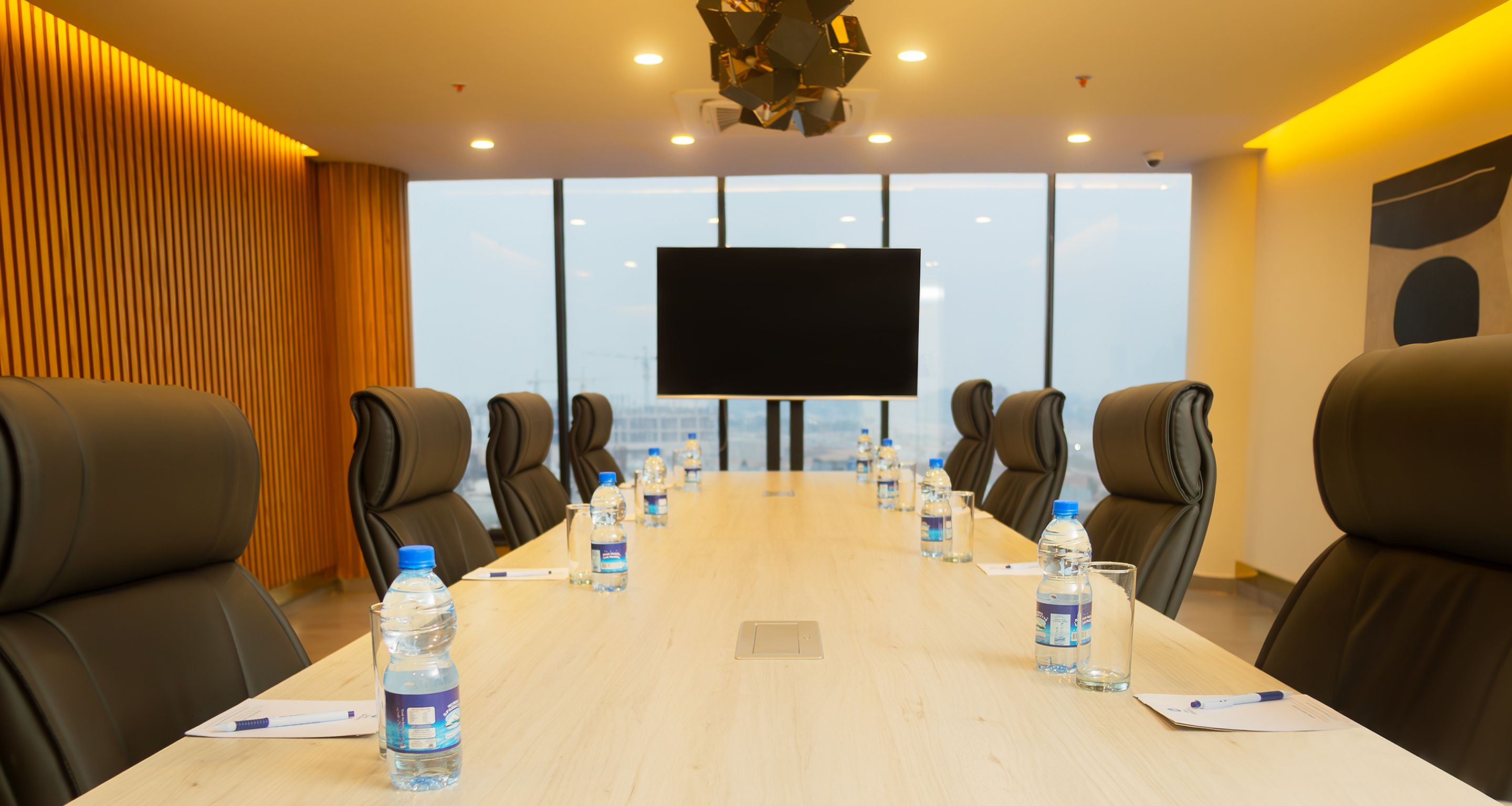 A conference room with a long table, multiple chairs, water bottles, and a large screen.