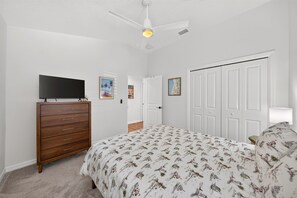 Ein Schlafzimmer mit Bett, Kommode, Fernseher und Deckenventilator.
