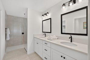 Un bagno moderno con due lavabi, uno specchio grande e una zona doccia.