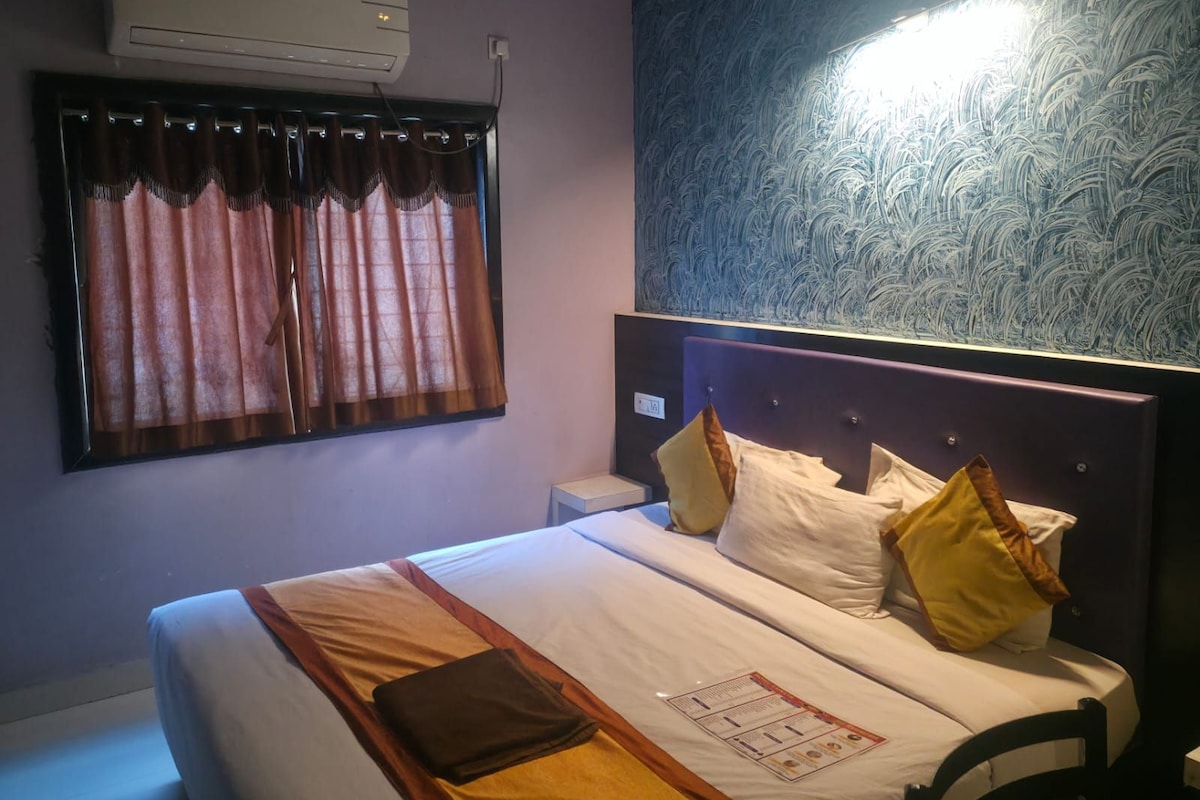 Una habitación de hotel con cama, mesita de noche, aire acondicionado de pared y ventana con cortinas.