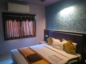 Una habitación de hotel con cama, mesita de noche, aire acondicionado de pared y ventana con cortinas.