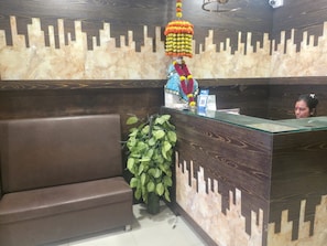 Un mostrador de recepción con una pared decorada, una planta en maceta y un sofá marrón.