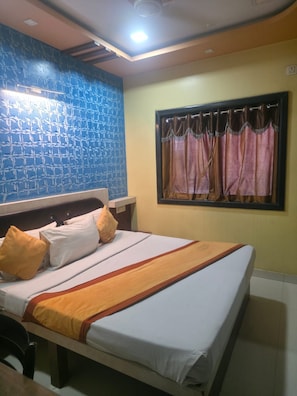Habitación de hotel con cama, almohadas, ventana con cortinas, pared con diseño azul y una lámpara en el techo.