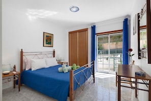 A hotel room with a bed, a nightstand, a table, a chair, a window with curtains, and a door.