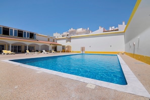 A swimming pool with a clear blue water surface, surrounded by a pebble ground and yellow and white walls.