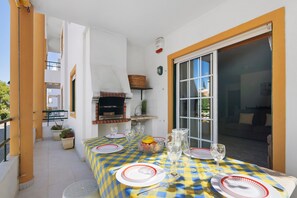 Et udendørs spiseområde med dug i tern, tallerkener, glas og en grill.