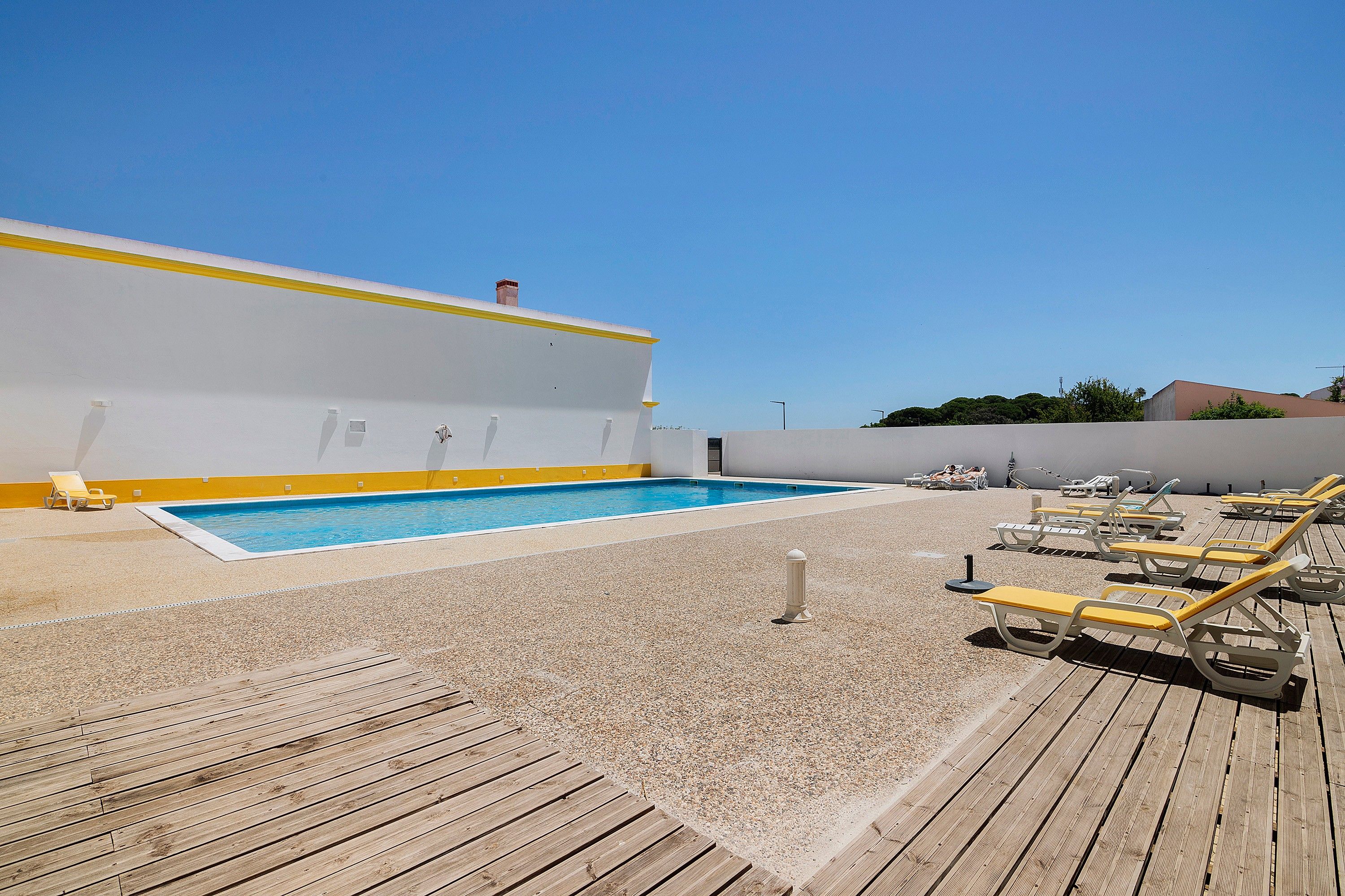 Ein Poolbereich auf dem Dach mit klarem, blauem Pool, Liegestühlen und einer Holzterrasse.