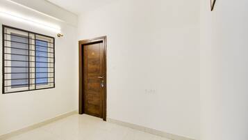 A hallway with a wooden door marked with the number 102, a window with metal bars, and a light switch on the wall.