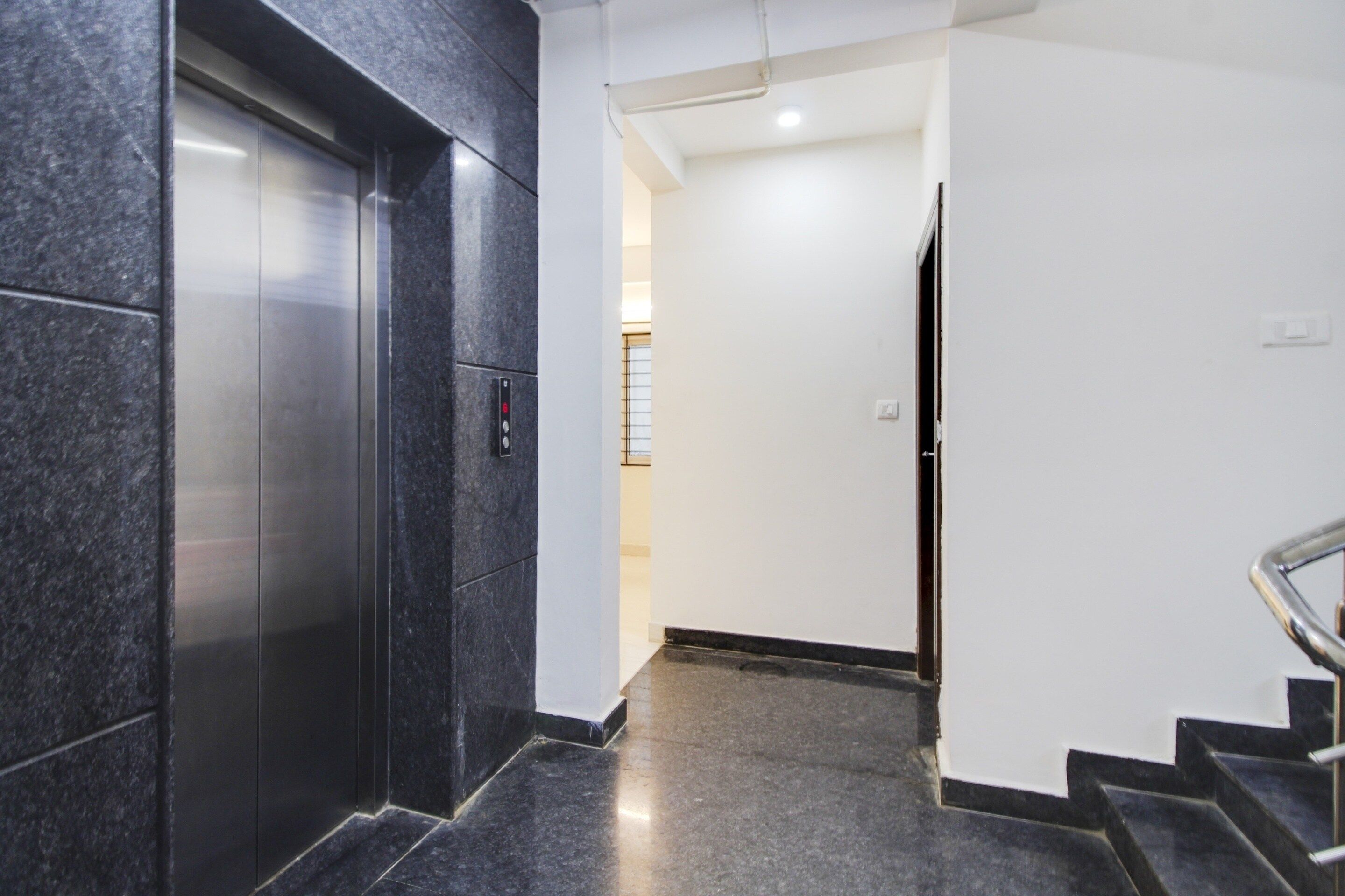 A modern elevator with a control panel, a staircase with a metal handrail, and a plain white wall.