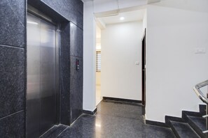 Un ascenseur moderne doté d’un panneau de commande, un escalier avec une rampe métallique et un mur blanc sobre.