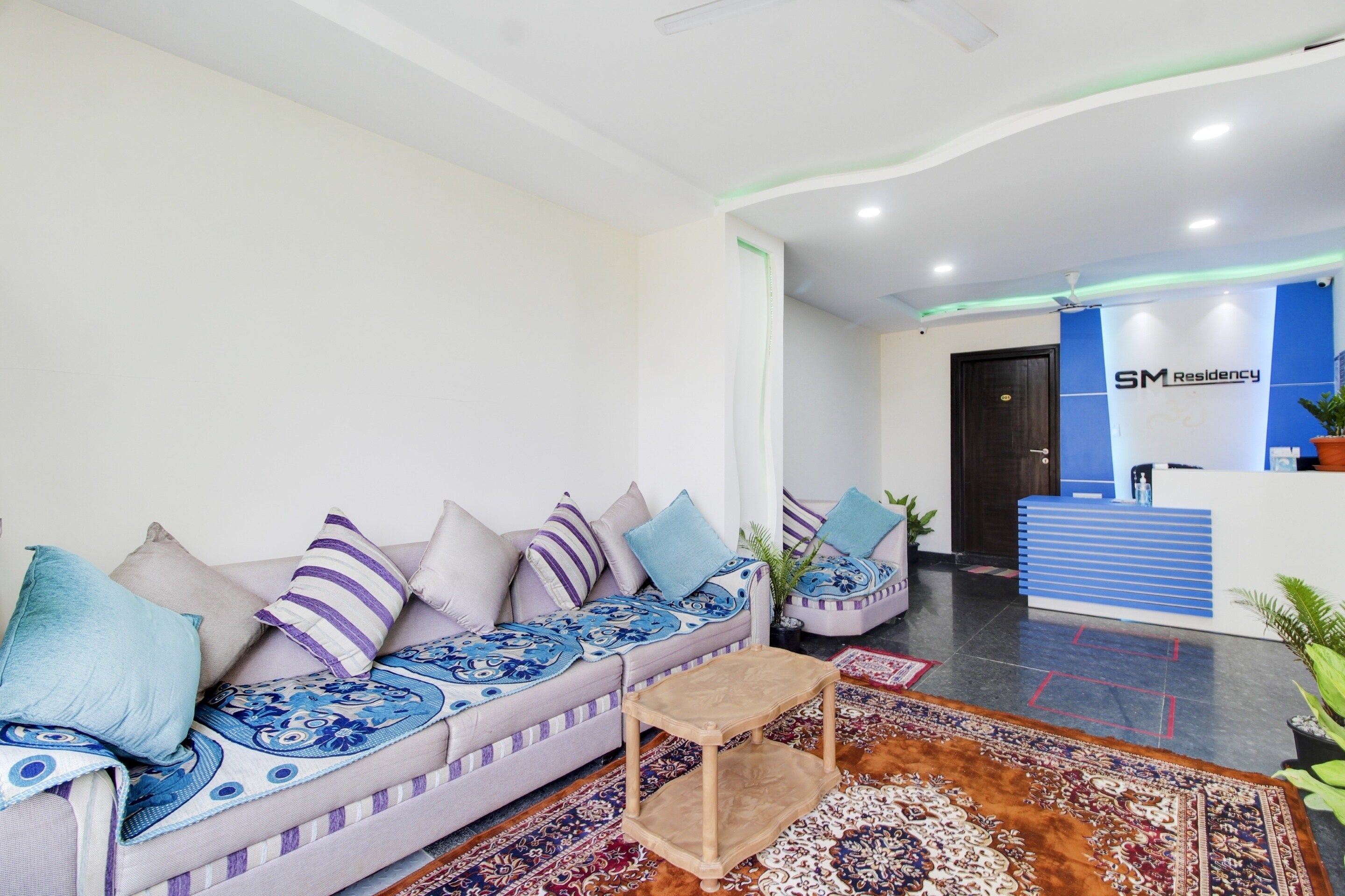 A modern hotel lobby with a sofa, a reception desk, and a patterned rug.