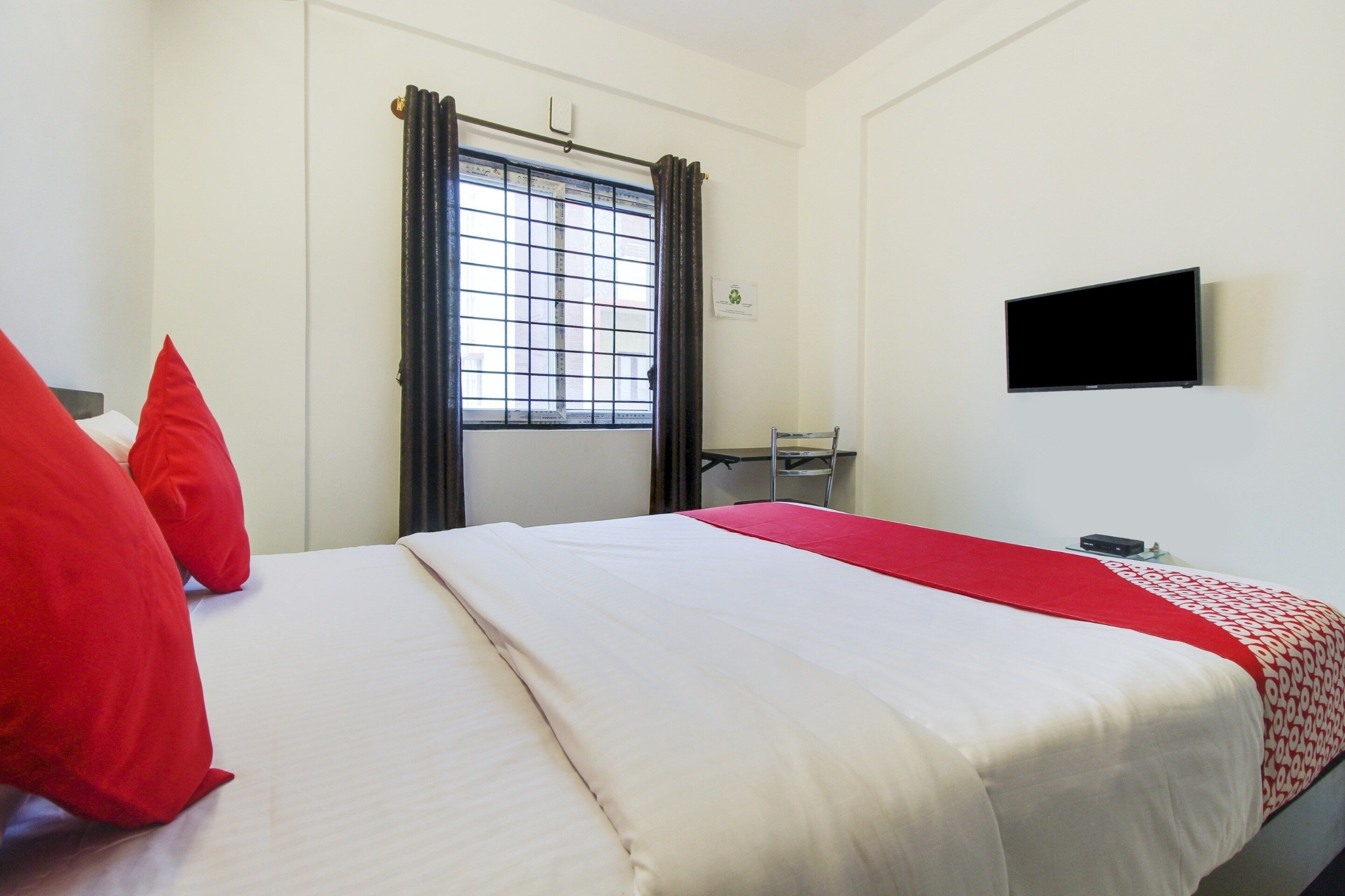 A hotel room with a bed, a TV, a window with curtains, and a chair.
